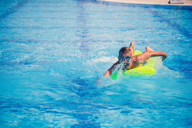 Apuesto joven nada en un colchón inflable en la piscina azul