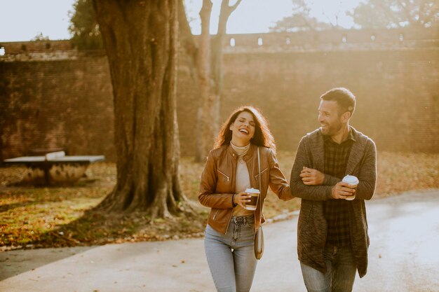 Apuesto joven pareja caminando en el parque otoño con café para llevar en las manos