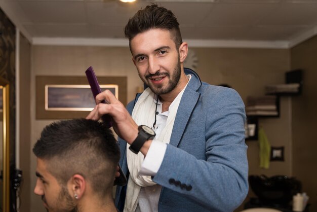 Apuesto joven peluquero dando un nuevo corte de pelo al cliente masculino en el salón