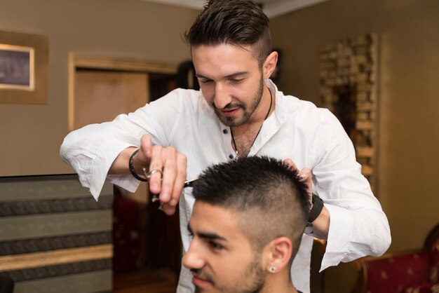 Apuesto joven peluquero dando un nuevo corte de pelo al cliente masculino en el salón