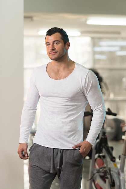 Apuesto joven de pie fuerte en camiseta blanca y flexionando los músculos Muscular culturista atlético modelo de fitness posando después de los ejercicios