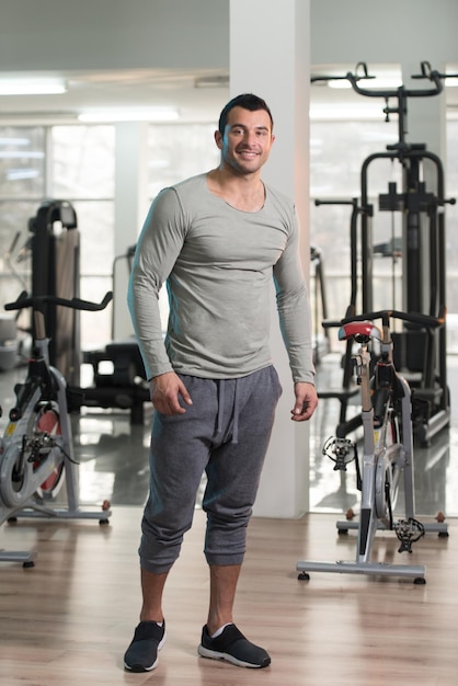 Apuesto joven de pie fuerte en camiseta verde Mangas largas y músculos flexibles Modelo de fitness culturista atlético muscular posando después de ejercicios