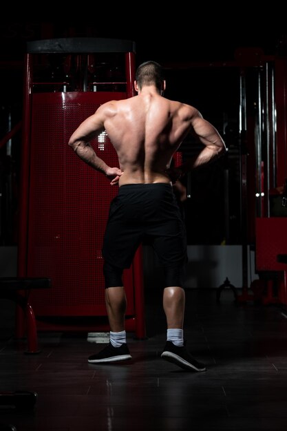 Apuesto joven de pie fuerte en el gimnasio y flexionando los músculos - Modelo de fitness culturista atlético muscular posando después de los ejercicios