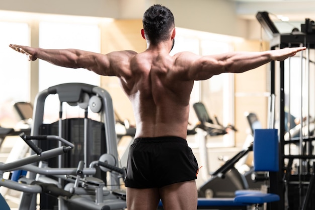 Apuesto joven de pie fuerte en el gimnasio y flexionando los músculos Muscular culturista atlético Modelo de fitness posando después de los ejercicios