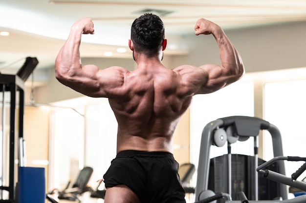 Apuesto joven de pie fuerte en el gimnasio y flexionando los músculos Muscular culturista atlético Modelo de fitness posando después de los ejercicios