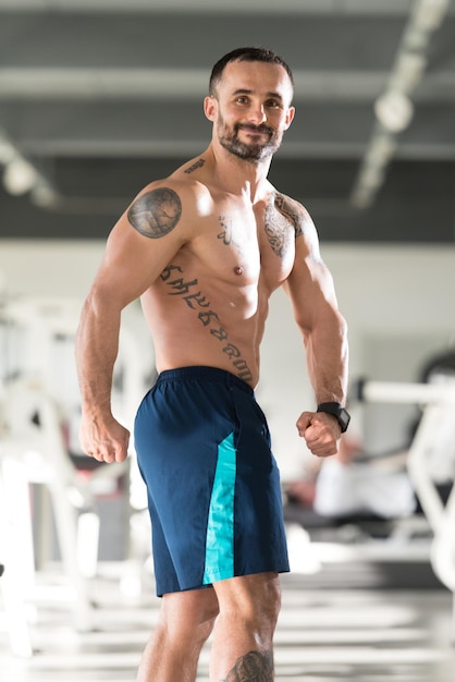 Apuesto joven de pie fuerte en el gimnasio y flexionando los músculos Muscular culturista atlético Modelo de fitness posando después de los ejercicios