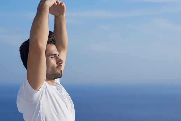 apuesto joven practicando yoga en la moderna terraza de la casa con el océano y la puesta de sol en el fondo