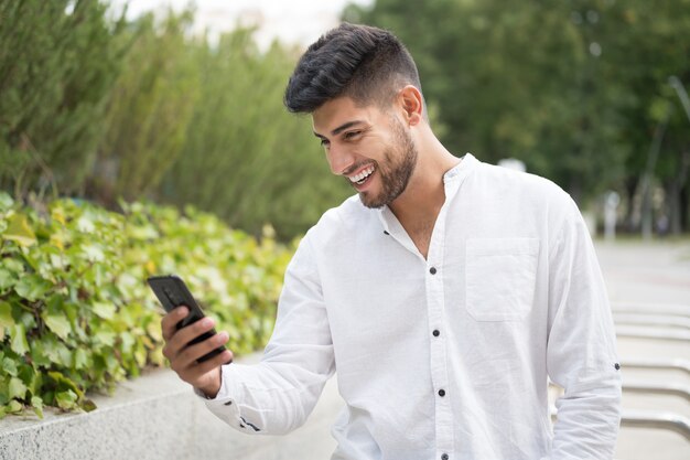 Apuesto joven de raza mixta sonriendo con un teléfono móvil al aire libre