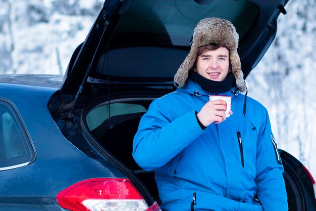 Apuesto joven en ropa de abrigo de invierno está bebiendo té o café bebida caliente