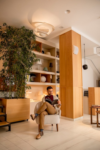 Foto apuesto joven en ropa casual y con anteojos leyendo un libro en casa