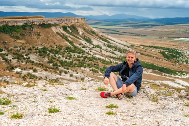 Apuesto joven rubio en un acantilado con vistas al paisaje rústico White Rock en Crimea