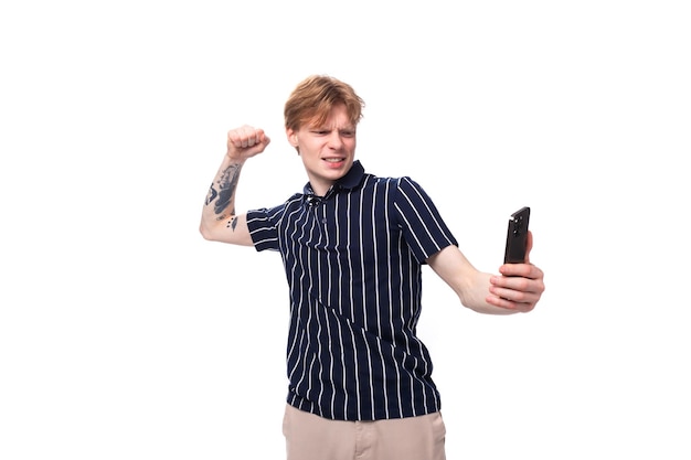 Un apuesto joven rubio con una camiseta sin mangas hace una foto por teléfono con un fondo blanco