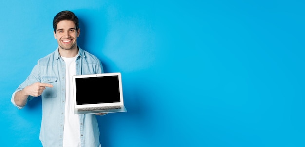 Apuesto joven señalando con el dedo a la pantalla de la computadora sonriendo complacido mostrando promoción en internet o