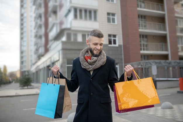 Apuesto joven sosteniendo muchas bolsas de la compra mientras está de pie en la calle