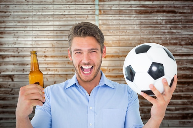 Apuesto joven sosteniendo pelota y cerveza contra tablones de madera