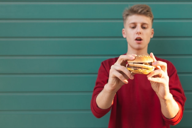 Apuesto joven sostiene una apetitosa hamburguesa en sus manos y la mira