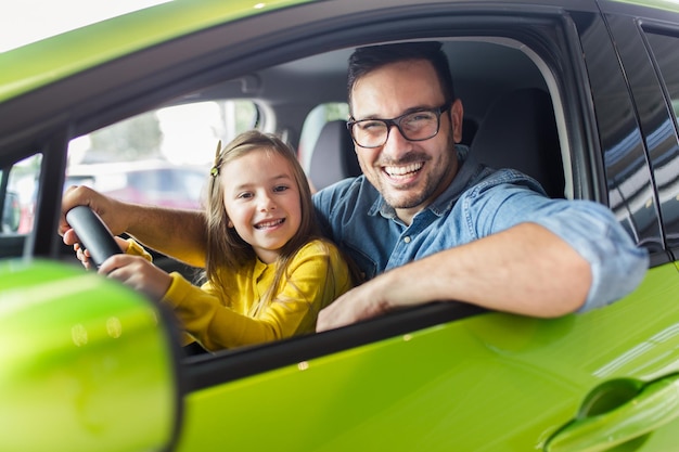 Apuesto joven con su linda hijita eligiendo un auto nuevo en la sala de exposición de autos.