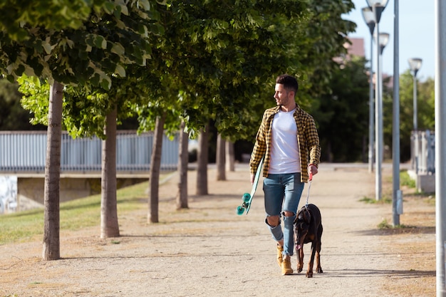 Apuesto joven con su perro caminando en el parque.