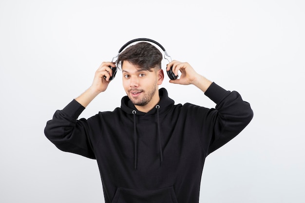 Apuesto joven en sudadera con capucha negra con grandes auriculares inalámbricos de música