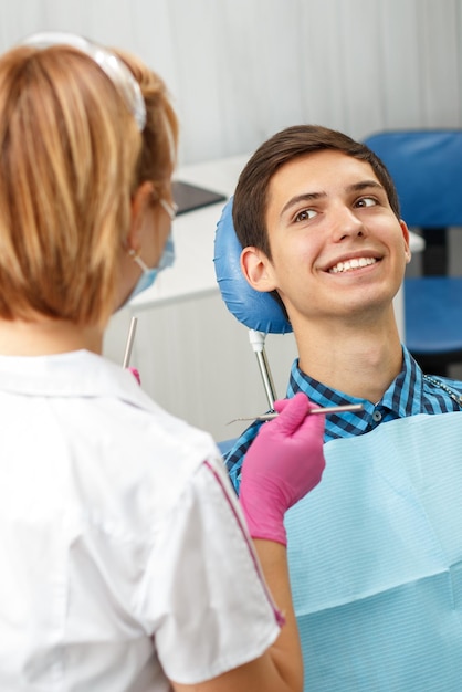 Apuesto joven tiene chequeo dental en consultorio dental. El dentista está examinando a un paciente con herramientas dentales