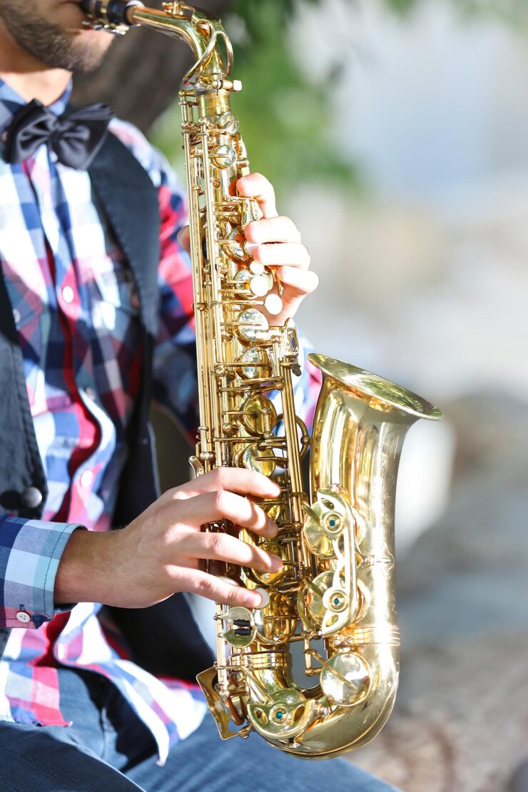 Foto apuesto joven toca el saxofón al aire libre de cerca