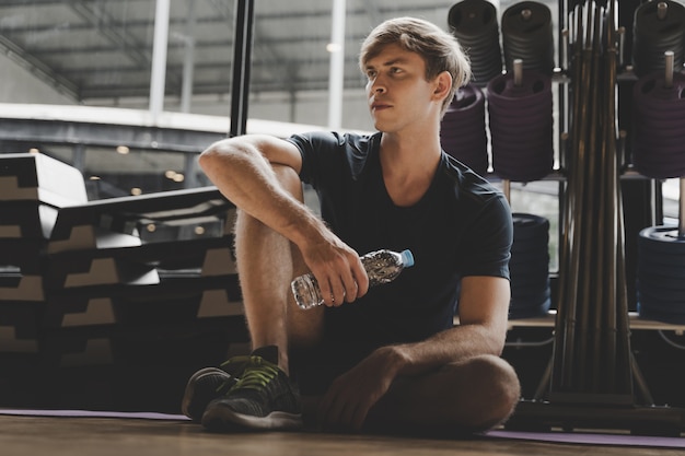 Apuesto joven tomando un descanso y descansando después del ejercicio en el gimnasio