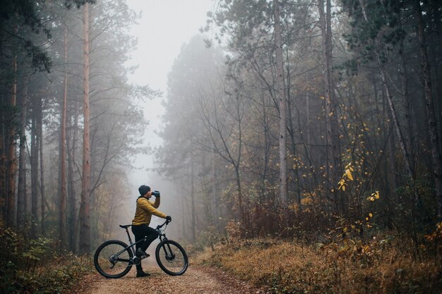 Apuesto joven tomando un freno durante el ciclismo a través del bosque de otoño