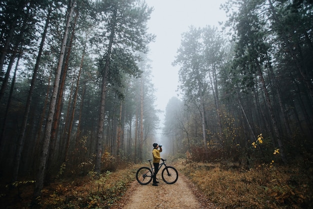 Apuesto joven tomando un freno durante el ciclismo a través del bosque de otoño