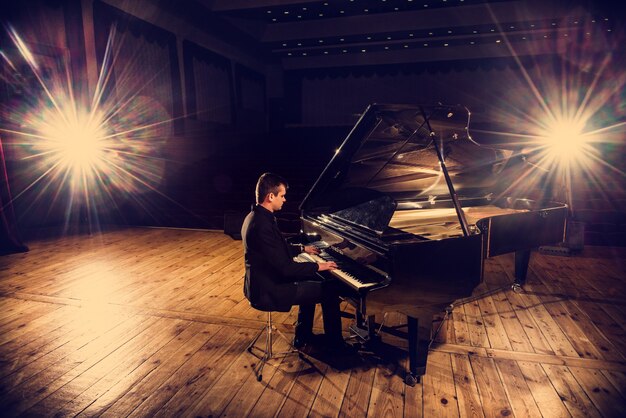 Apuesto joven en traje está sentado al piano y haciendo música de piano.