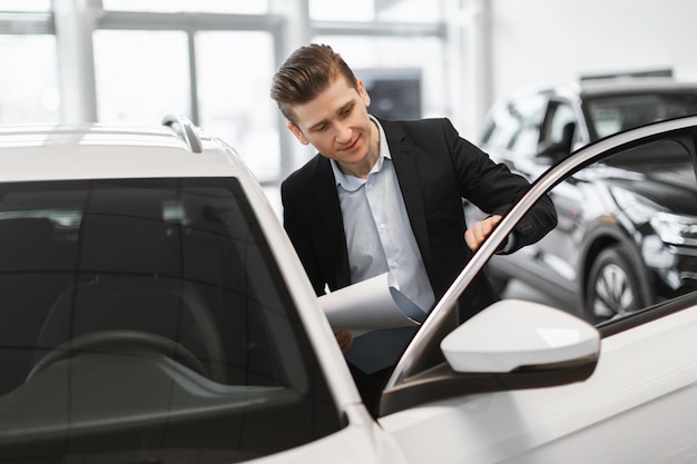 Apuesto joven vendedor de autos revisando el automóvil antes de venderlo en el centro de concesionarios