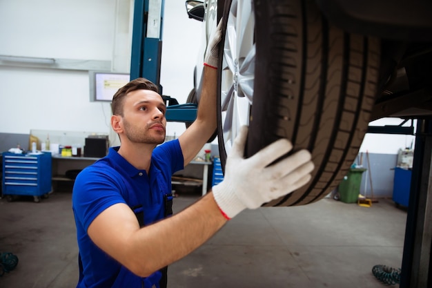 Apuesto mecánico de automóviles profesional cambia una rueda de un automóvil o realiza un cambio de llanta en un centro de reparación de automóviles especializado