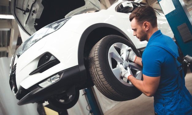 Apuesto mecánico de automóviles profesional cambia una rueda de un automóvil o realiza un cambio de llanta en un centro de reparación de automóviles especializado