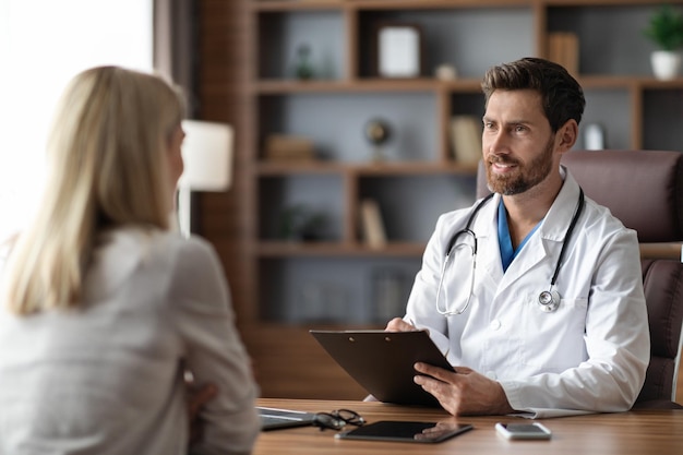 Apuesto médico masculino en consulta uniforme paciente femenino durante la reunión en la clínica