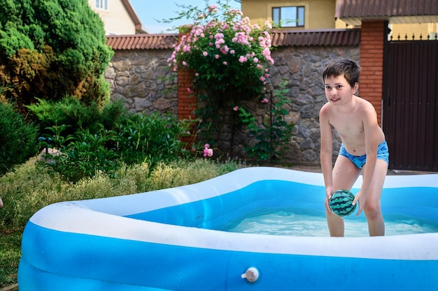 Un apuesto niño caucásico en edad escolar juega con una pelota flotante mientras nada en la piscina inflable en un día soleado de verano