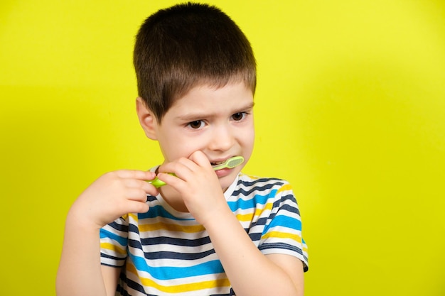 Un apuesto niño preescolar se cepilla los dientes con un fondo amarillo
