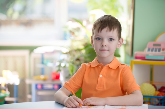 Un apuesto niño de seis años en una mesa con un lápiz y un cuaderno.