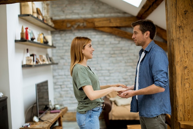 Apuesto novio amoroso sonriendo mientras toma las manos de la novia en un apartamento tipo loft