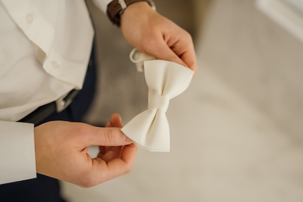 El apuesto novio que se ata la corbata de lazo en la mañana del día de la boda. Preparación de la boda del novio.