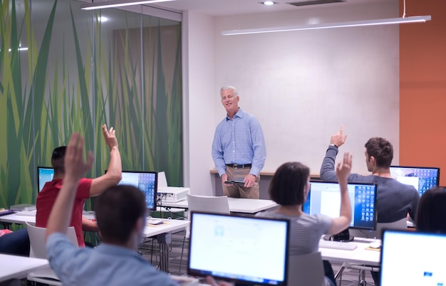 Apuesto profesor maduro y estudiantes en el aula de laboratorio de computación