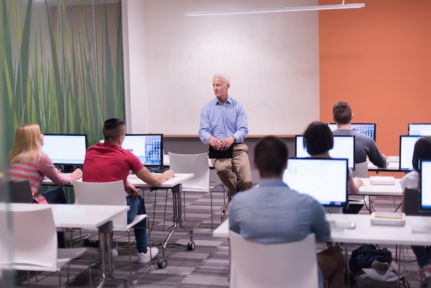 Apuesto profesor maduro y estudiantes en el aula de laboratorio de computación