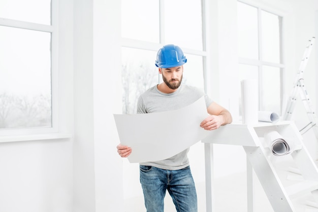 Apuesto reparador o constructor en casco trabajando con dibujos sobre la renovación del interior del apartamento