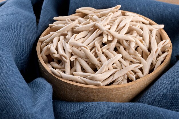 Apulische Vollkornnudeln Pizzarieddi oder Maccaruni in einem Sieb auf blauer Leinenserviette. Typisches Gericht der frischen Maccheroni von Apulien Salento Italien. Italienische hausgemachte Pasta Hintergrund, Nahaufnahme