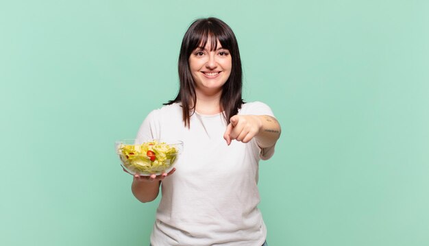 apuntando a la cámara con una sonrisa satisfecha, confiada y amistosa, eligiéndote