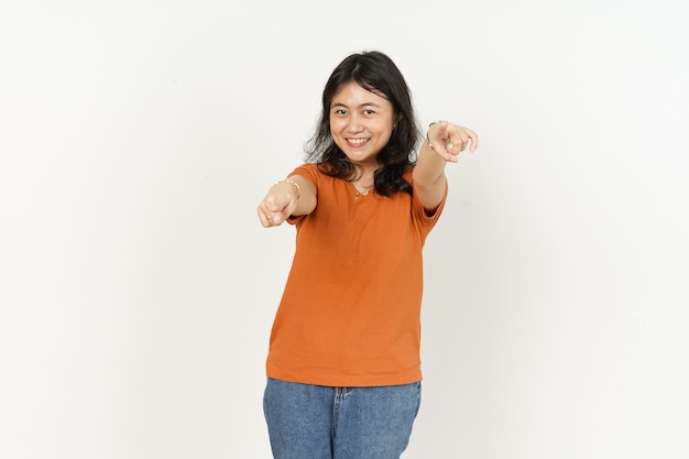 Apuntando a usted de hermosa mujer asiática vistiendo camiseta naranja aislado sobre fondo blanco.