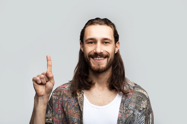 Apunte los dedos sobre su cabeza con una cara sonriente para colocar texto, logotipo o publicidad. Hipster viajero elegante hombre despreocupado sobre un fondo blanco de estudio, estilo de vida de las personas