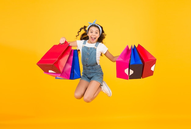 Apure su venta total. Moda infantil. Ventas y descuentos. niña feliz después de compras exitosas. niño enérgico salto con bolsas pesadas. regalos navideños en paquetes. lunes cibernético. Tiempo de compras.