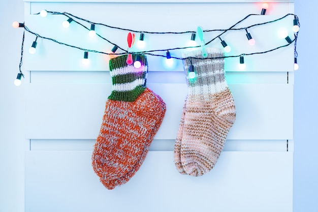 Foto aqueça as peúgas feitas malha do inverno que penduram em luzes de natal de uma iluminação em casa.