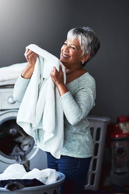 Foto aquele cheiro de amaciante de tecido lindamente perfumado foto de uma mulher madura cheirando toalhas recém-lavadas enquanto lavava roupa em casa
