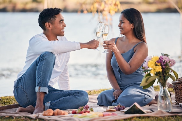Aquí está el amor eterno Fotografía de una pareja joven que hace un brindis mientras disfruta de un picnic a la orilla de un lago