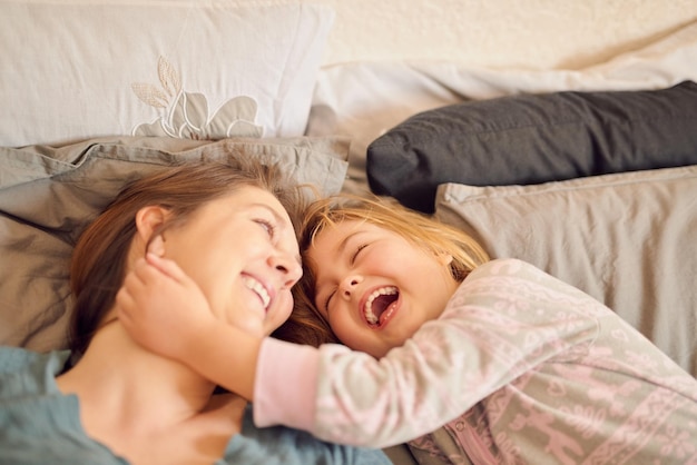 Aquí viene el monstruo de las cosquillas Disparo de una madre y su hijita acostadas juntas en la cama en casa